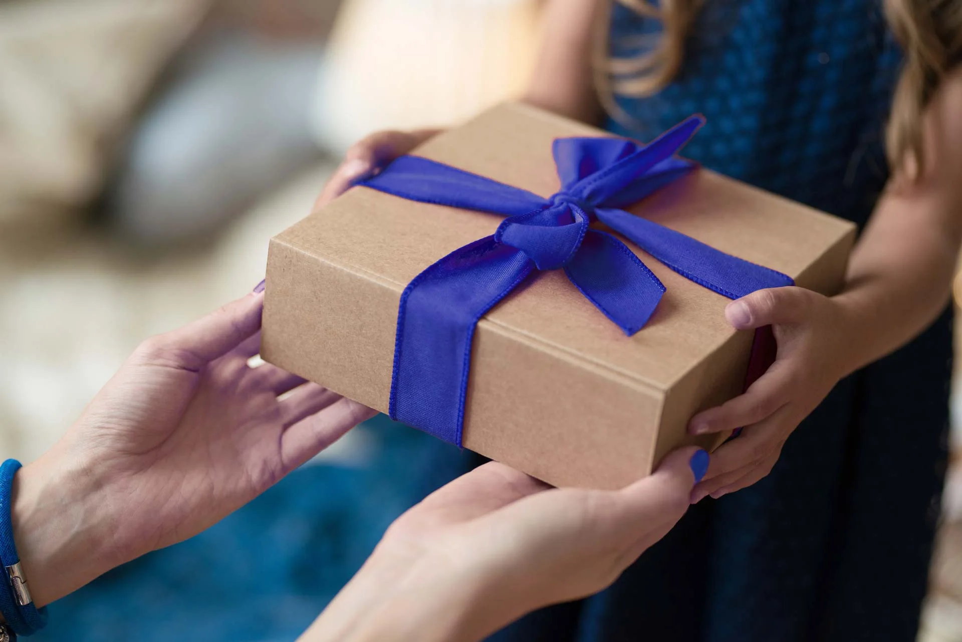 In the picture there are two hands offering a brown gift package with a blue bow to a little girl.