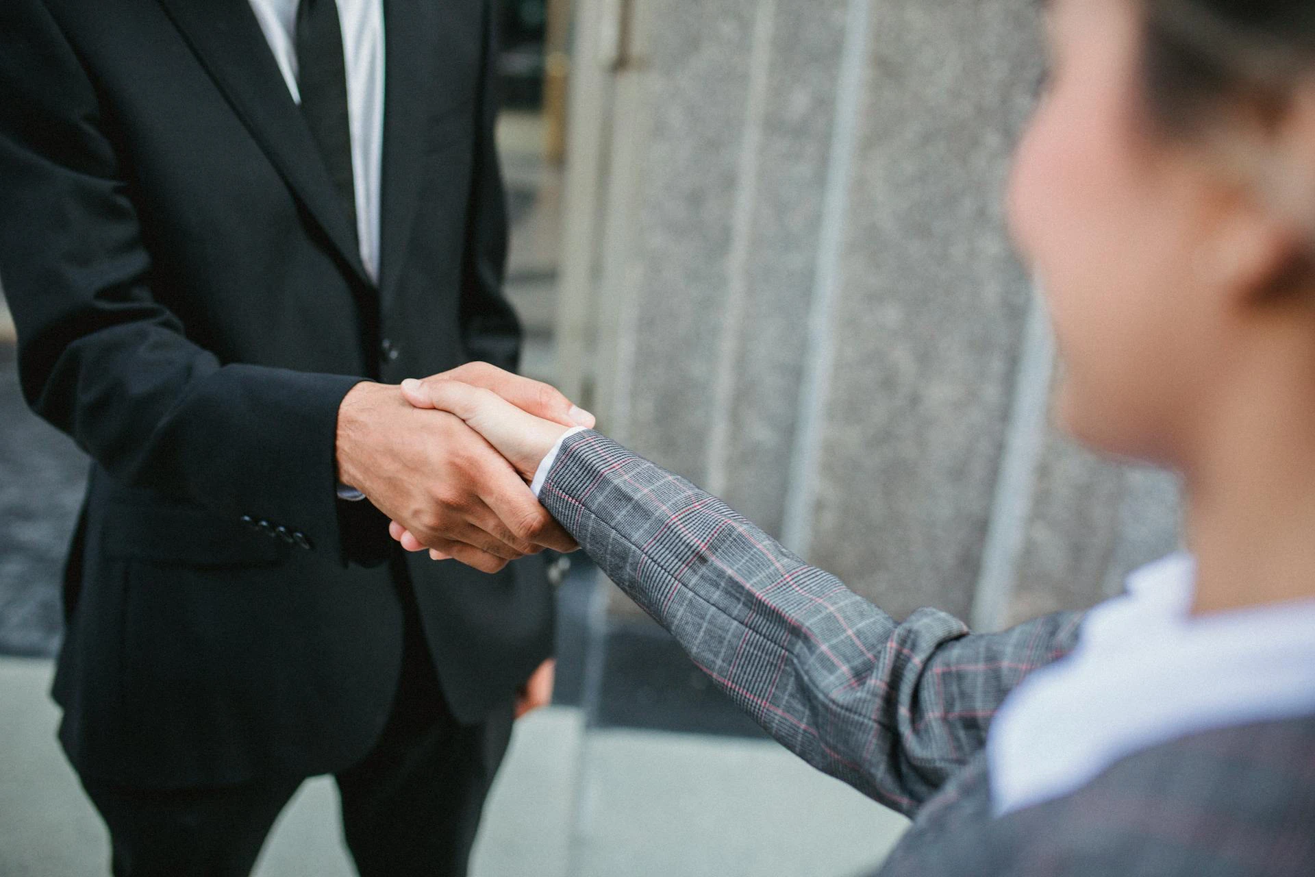The image shows a woman and a man shaking hands. Both are dressed in formal attire.