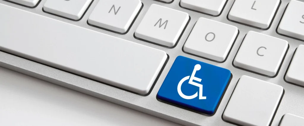 In the image there is a white keyboard where one of the keys has been replaced by a white icon on a blue background with the symbol of a disabled person in a wheelchair
